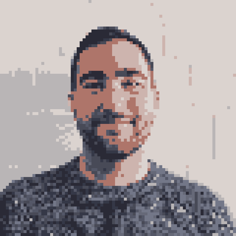 A white guy wearing a blue sweater in front of a white wall, pixelated